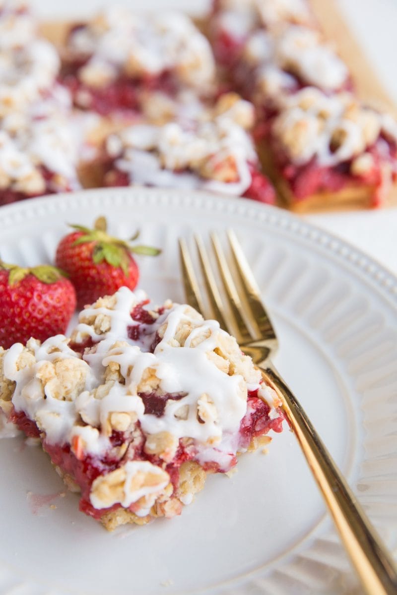 strawberry oatmeal bar on a plate with a gold fork and bars in the background