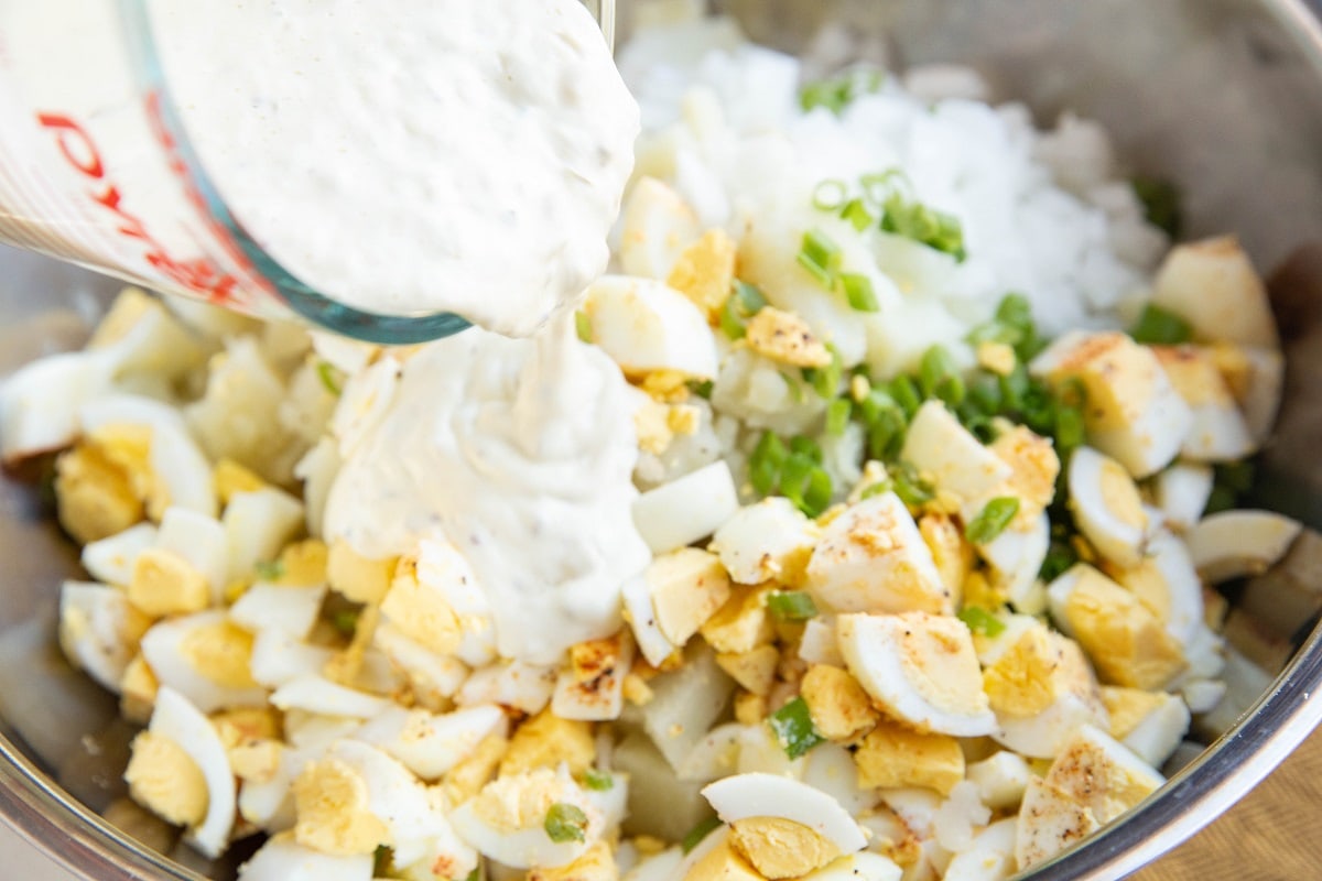 Dressing being poured over potato salad ingredients.