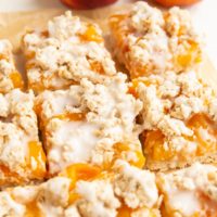 parchment paper with slices of peach pie bars on top and peaches in the background