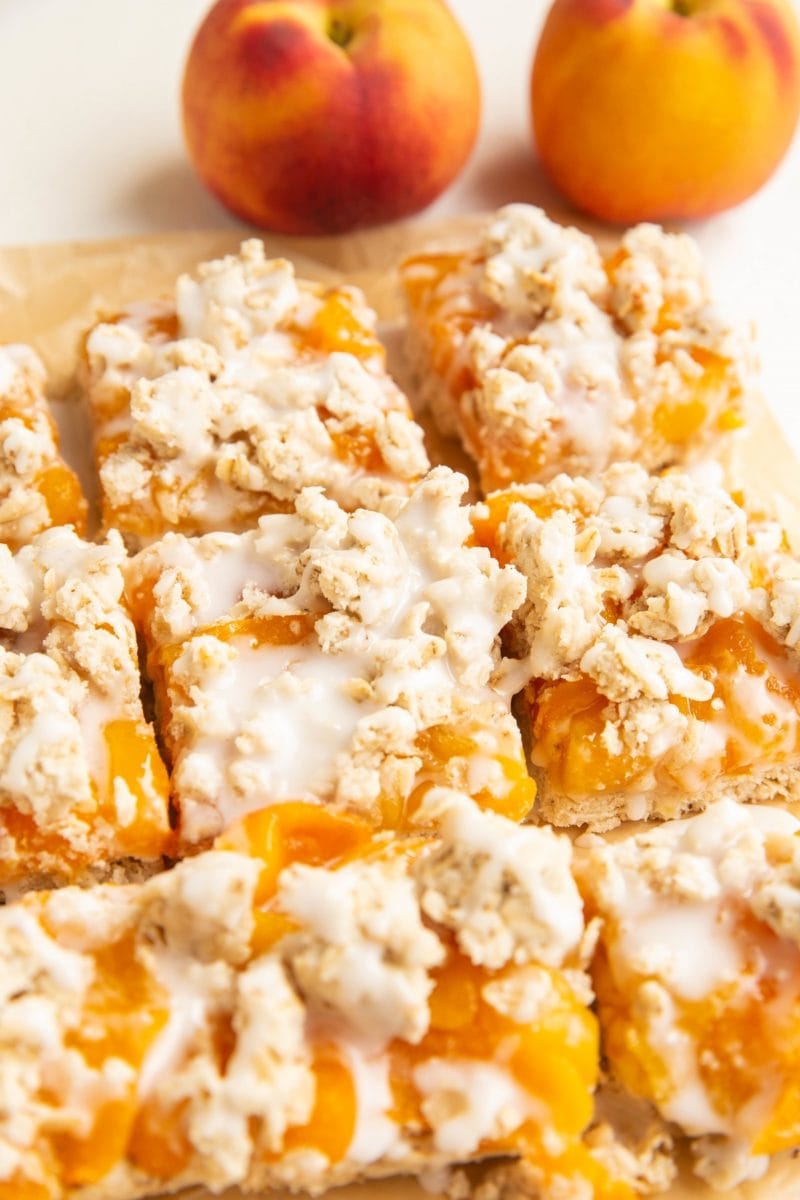 parchment paper with slices of peach pie bars on top and peaches in the background