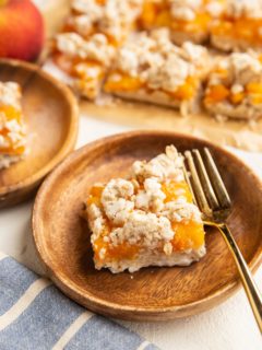two wooden plates with slices of peach pie bars and more pie bars in the background