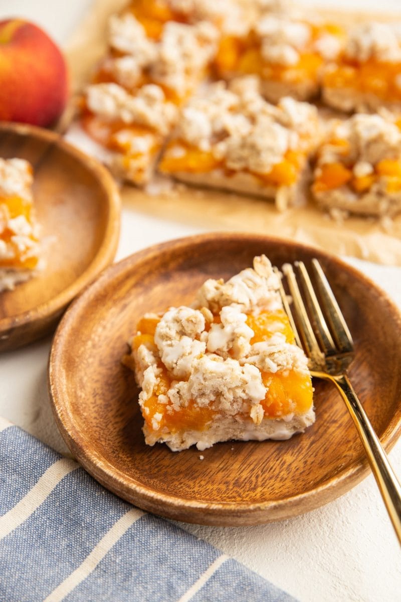 two wooden plates with slices of peach pie bars and more pie bars in the background