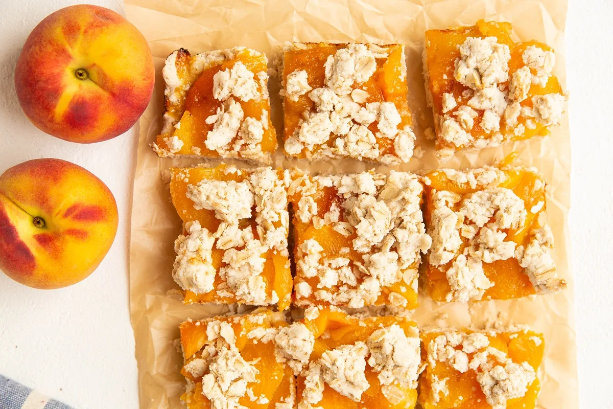 Easy Peach Pie Bars on a sheet of parchment paper with fresh peaches to the side