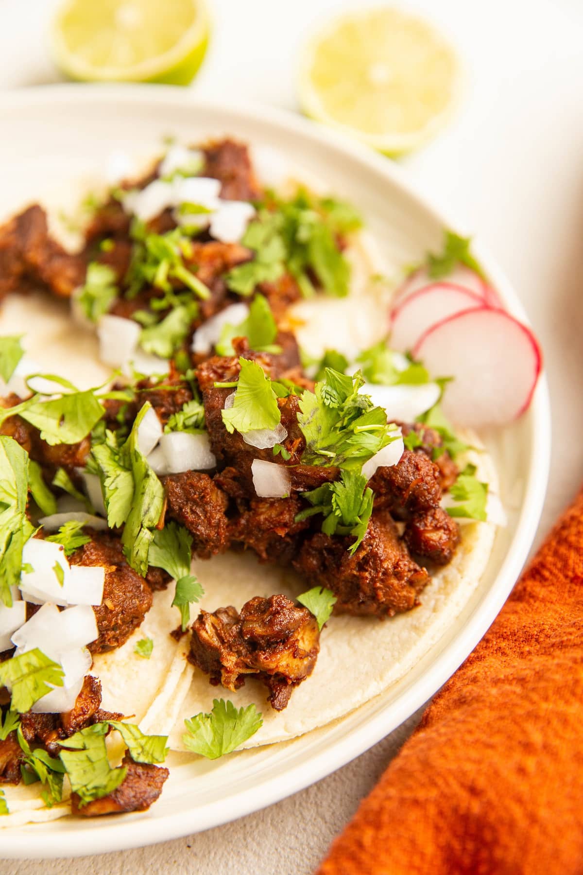 white plate with al pastor tacos with fresh cilantro and onion on top