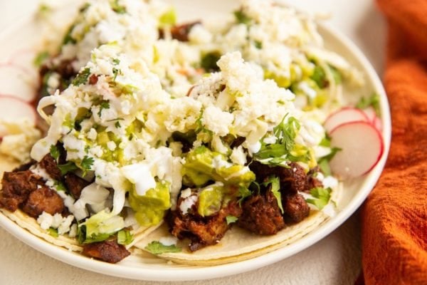 Plate of al pastor tacos with slaw, guacamole, cheese, and salsa