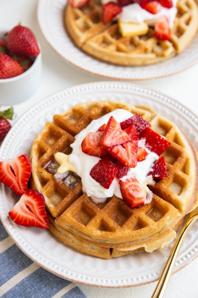 two white plates of Belgian waffles with fresh berries and whipped cream