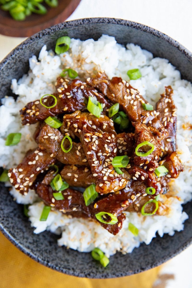 Close up top down photo of bulgogi beef on a bed of white rice with sesame seeds and green onions