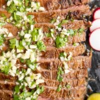 Carne Asada sliced on a black cutting board with garlic and cilantro on top