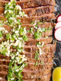 Carne Asada sliced on a black cutting board with garlic and cilantro on top