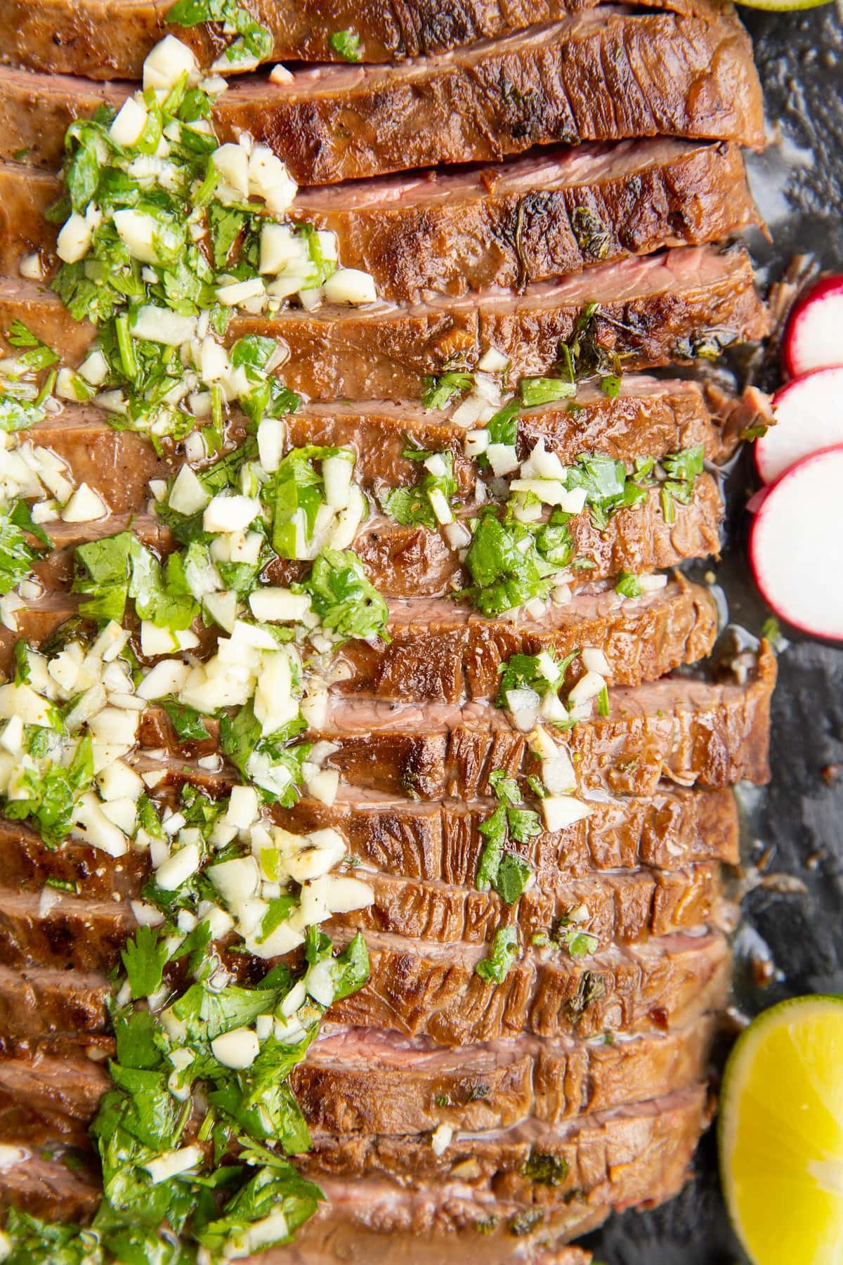 Carne Asada sliced on a black cutting board with garlic and cilantro on top