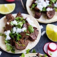 Carne Asada tacos on a black slate with sliced turnips and limes