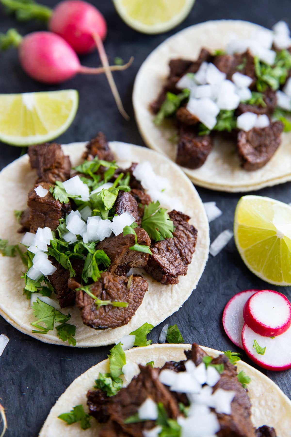 Carne Asada tacos on a black slate with sliced turnips and limes