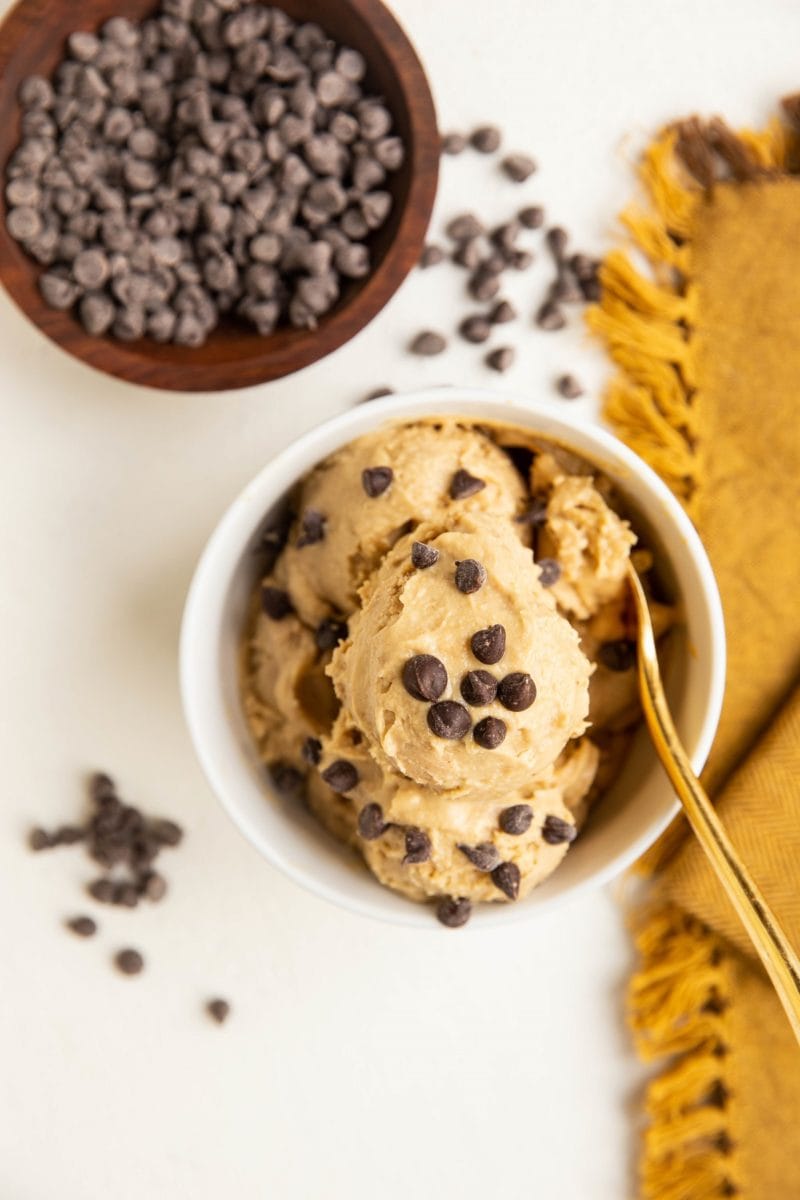 Top down photo of chickpea ice cream in a white bowl with a golden napkin to the side and chocolate chips sprinkled around.