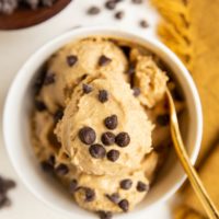 Peanut Butter Banana Chickpea Ice Cream in a white bowl with a golden spoon and chocolate chips all around.