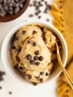 Peanut Butter Banana Chickpea Ice Cream in a white bowl with a golden spoon and chocolate chips all around.