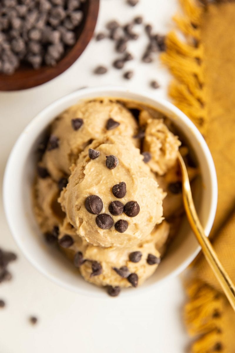 Peanut Butter Banana Chickpea Ice Cream in a white bowl with a golden spoon and chocolate chips all around.