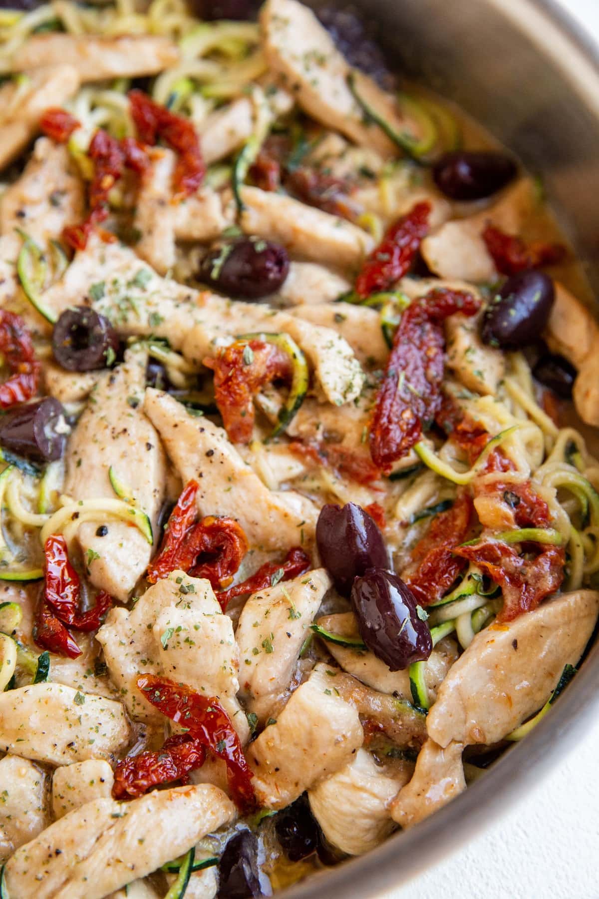 close up skillet of creamy Mediterranean Chicken with sun-dried tomato sauce and zoodles