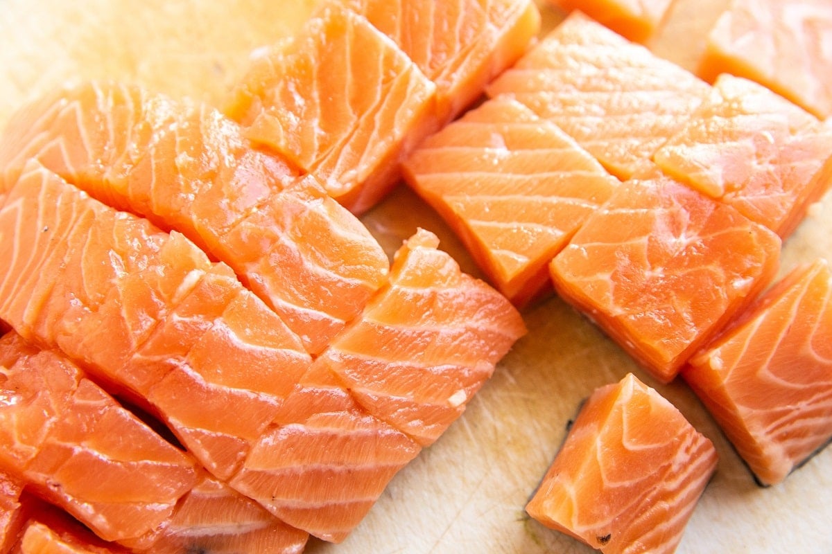 Chopped salmon on a cutting board, cut into bite sized cubes.