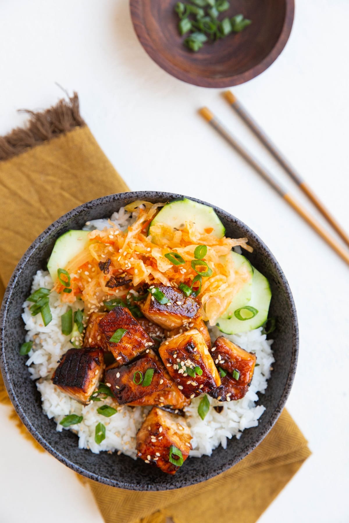 Bowl of asian salmon on top of a golden napkin with chopsticks to the side.