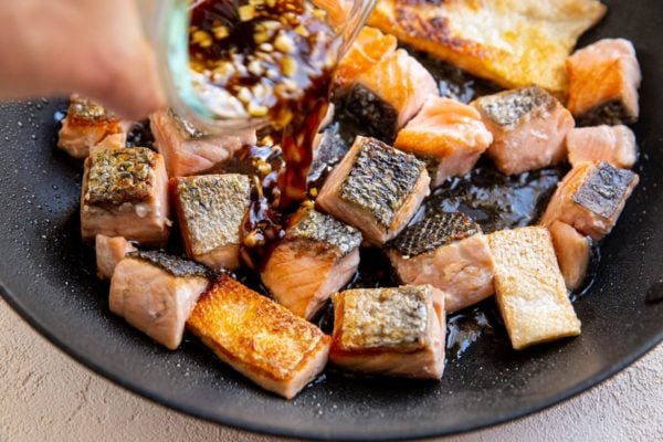 Pouring sweet Asian sauce into the skillet with salmon