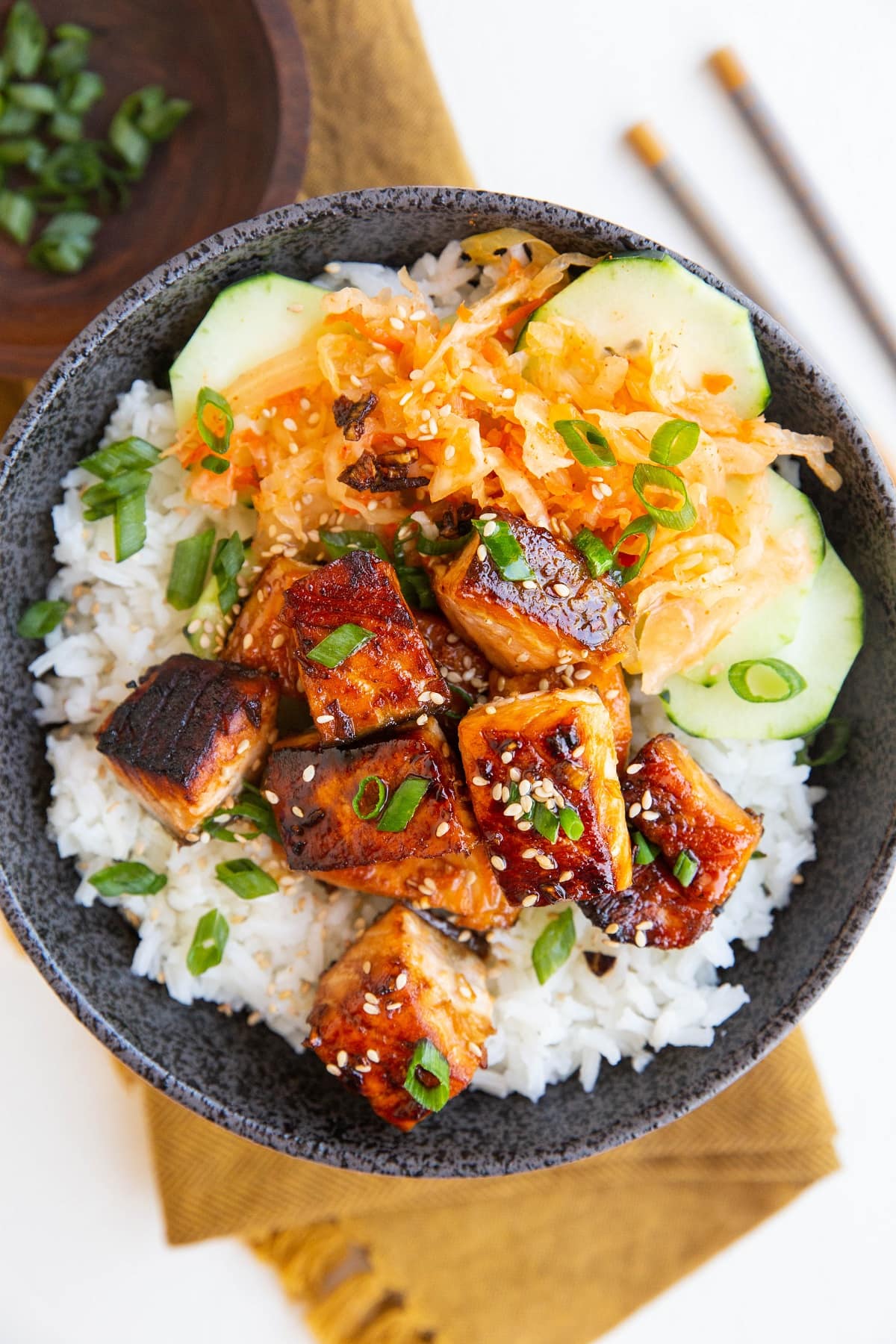 Cooked salmon in a bowl with white rice, sauerkraut and cucumber salad