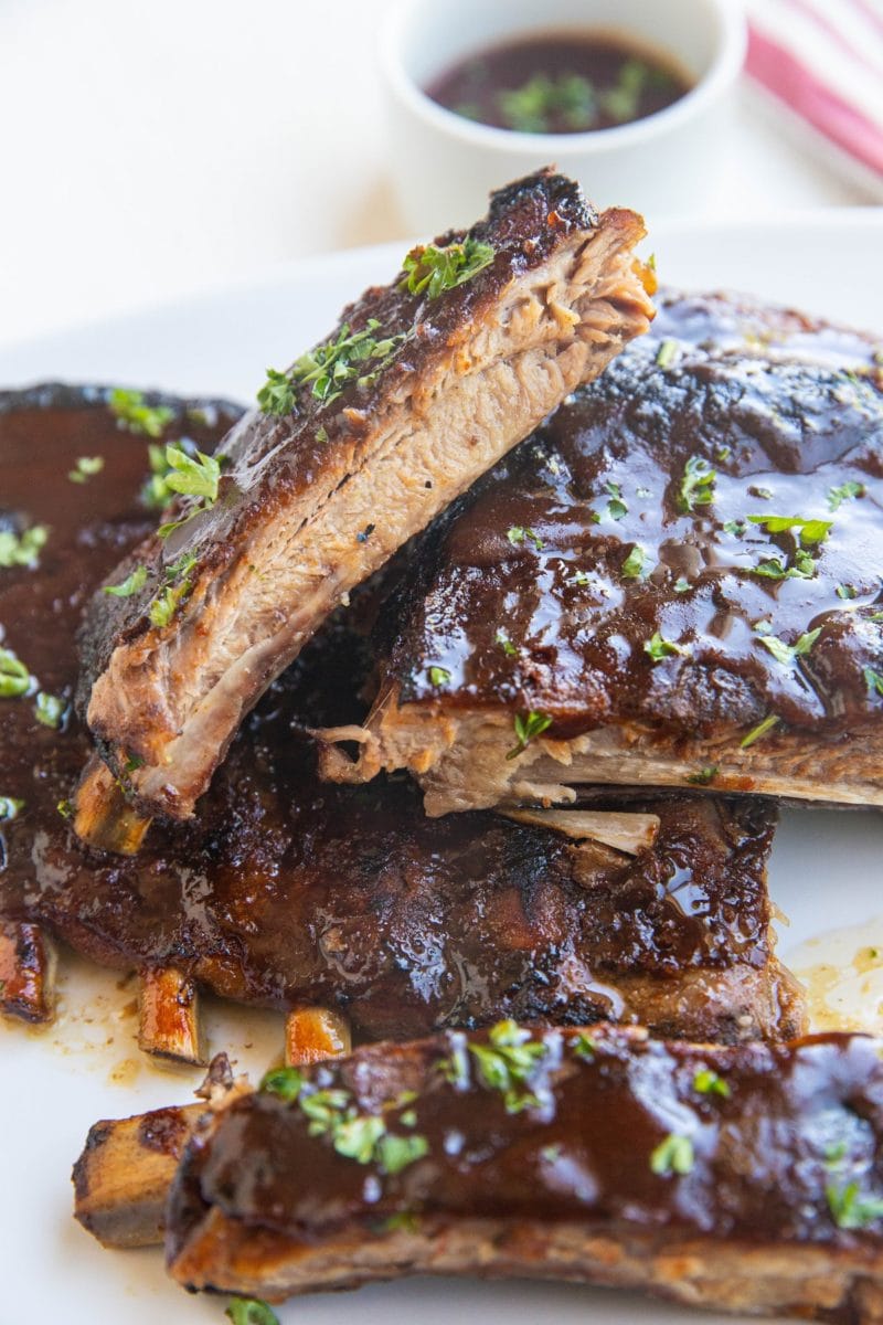 Slow Cooker ribs on a plate, sliced into individual ribs with bbq sauce for dipping