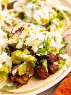 close up image of al pastor tacos on a plate with toppings