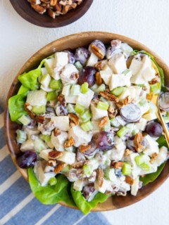 wooden bowl of chicken salad on a bed of butter lettuce with a blue striped napkin and a wooden bowl of pecans