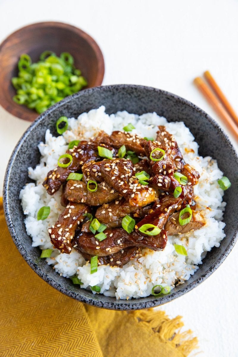 bowl of korean beef with golden napkin, chopsticks and a bowl of green onions