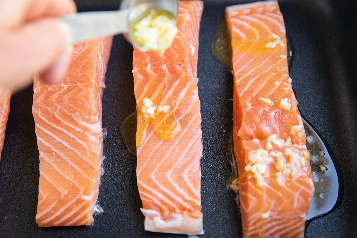 Drizzling butter and garlic over raw salmon filets