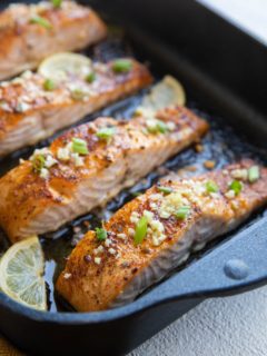 roasting pan with four baked salmon fillets sprinkled with garlic and green onion