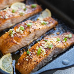 roasting pan with four baked salmon fillets sprinkled with garlic and green onion