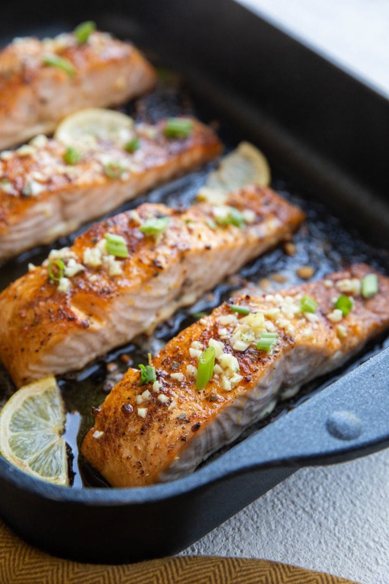 roasting pan with four baked salmon fillets sprinkled with garlic and green onion