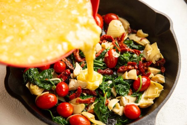 Pouring egg mixture over the greek frittata ingredients