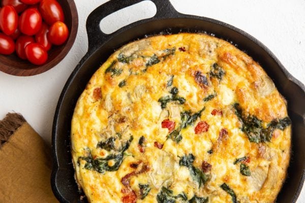 cast iron skillet with frittata and a bowl of cherry tomatoes