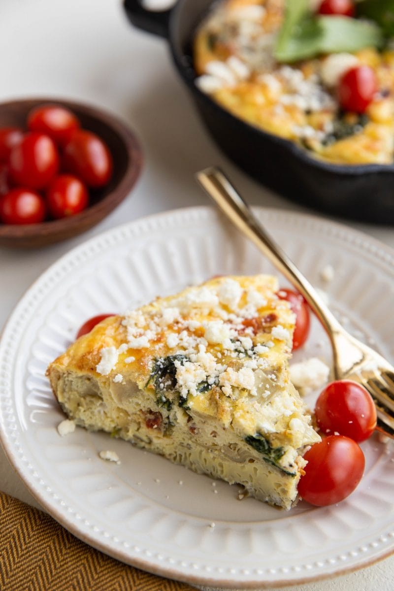 greek frittata on a white plate with skillet of frittata in the background