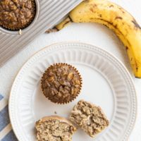 plate of baked oatmeal muffins and a muffin tray with baked muffins inside. A blue napkin to the side and a ripe banana