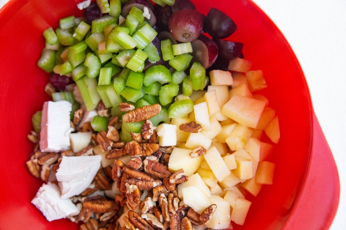Chicken, apples, pecans, grapes, and celery in a mixing bowl.