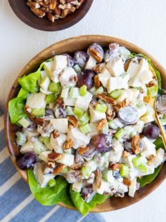 wooden bowl of chicken salad on a bed of butter lettuce with a blue striped napkin and a wooden bowl of pecans