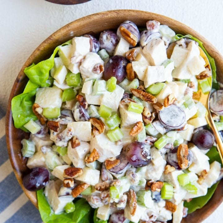 wooden bowl of chicken salad on a bed of butter lettuce with a blue striped napkin and a wooden bowl of pecans