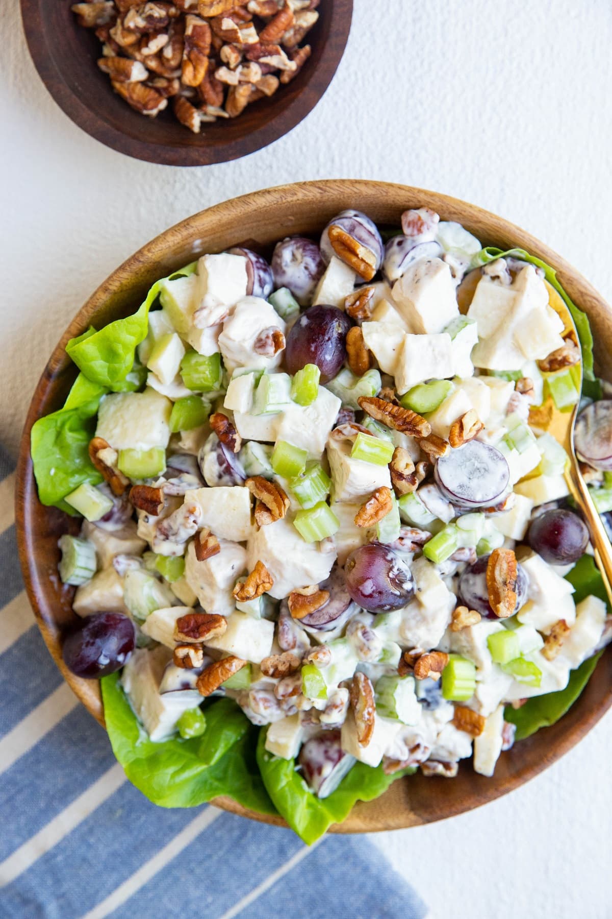 wooden bowl of chicken salad on a bed of butter lettuce with a blue striped napkin and a wooden bowl of pecans