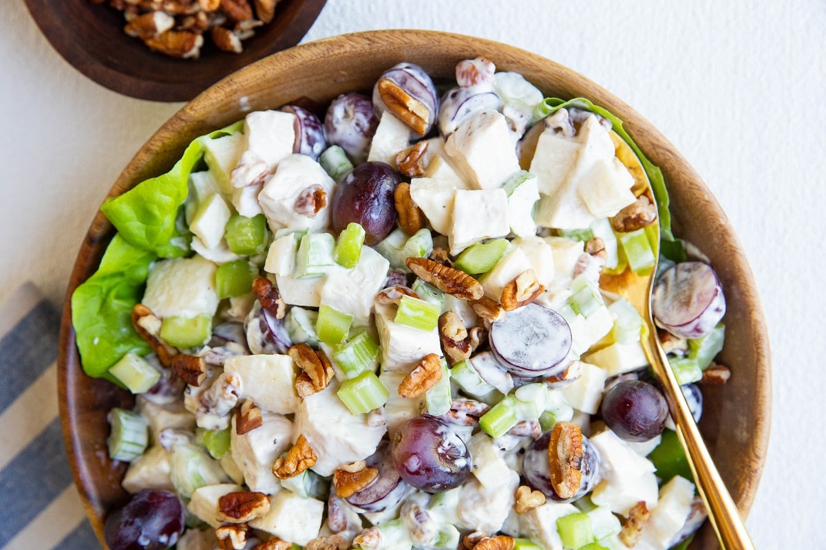 horizontal wooden bowl of chicken salad with a golden spoon and a blue napkin.