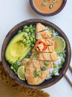 wooden bowl of chicken katsu with white rice, avocado, edamame and sauce