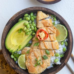 wooden bowl of chicken katsu with white rice, avocado, edamame and sauce