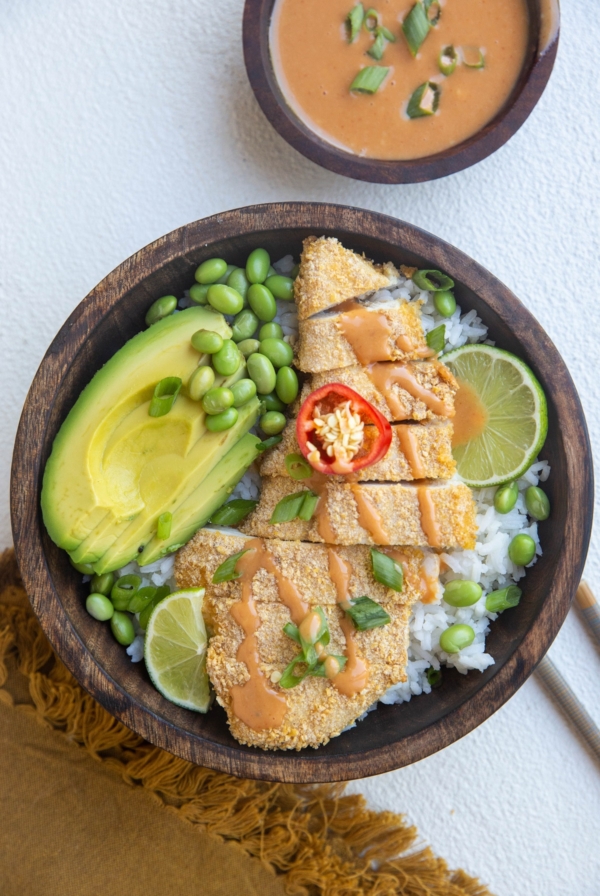 wooden bowl of chicken katsu with white rice, avocado, edamame and sauce
