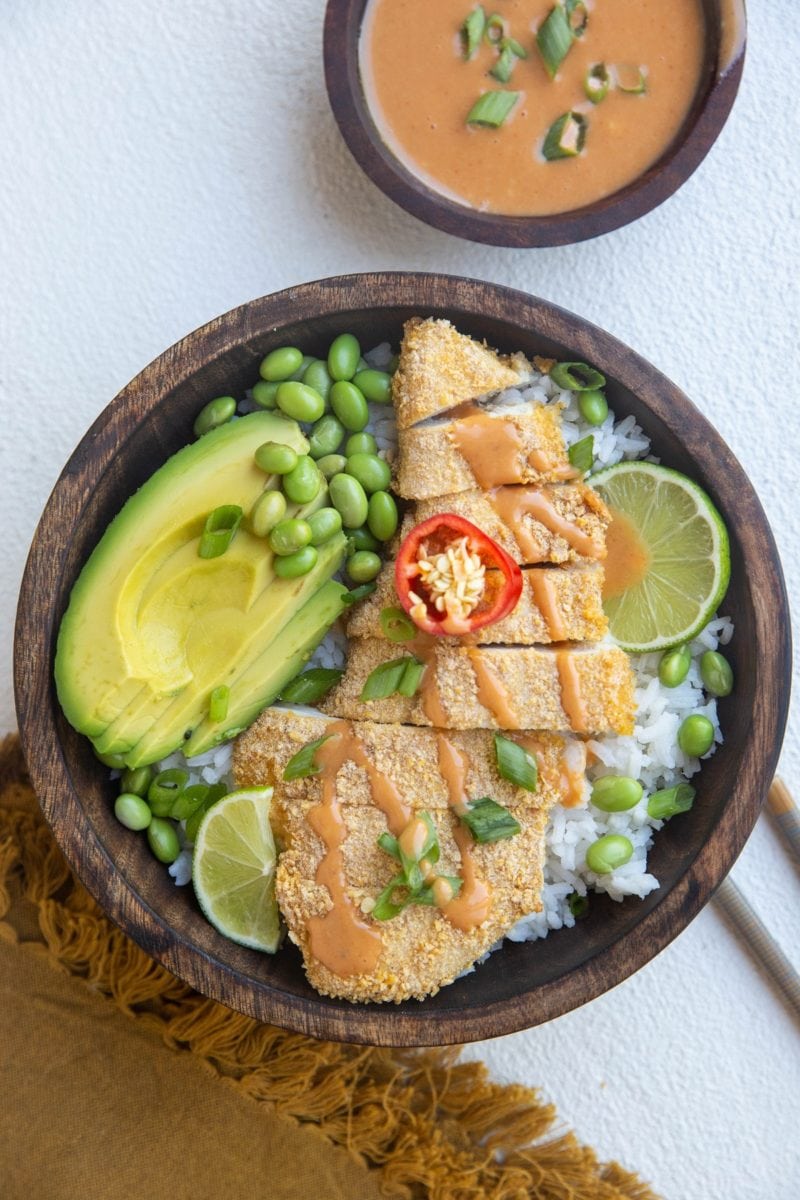 wooden bowl of chicken katsu with white rice, avocado, edamame and sauce