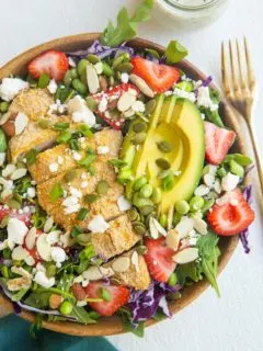 bowl of crispy chicken salad with strawberries. blue napkin and gold fork off to the side.