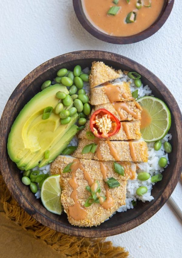 wooden bowl of chicken katsu with white rice, avocado, edamame and sauce