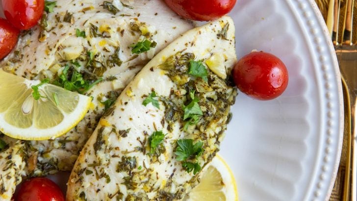 Two chicken breasts on a white plate with cherry tomatoes, sliced lemons and golden napkin