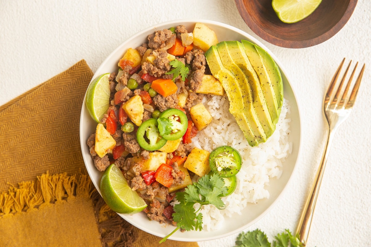 horizontal photo of picadillo in a bowl with white rice, avocado and cilantro